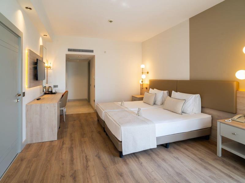 Modern hotel room with double bed, flat-screen TV, and wooden flooring.
