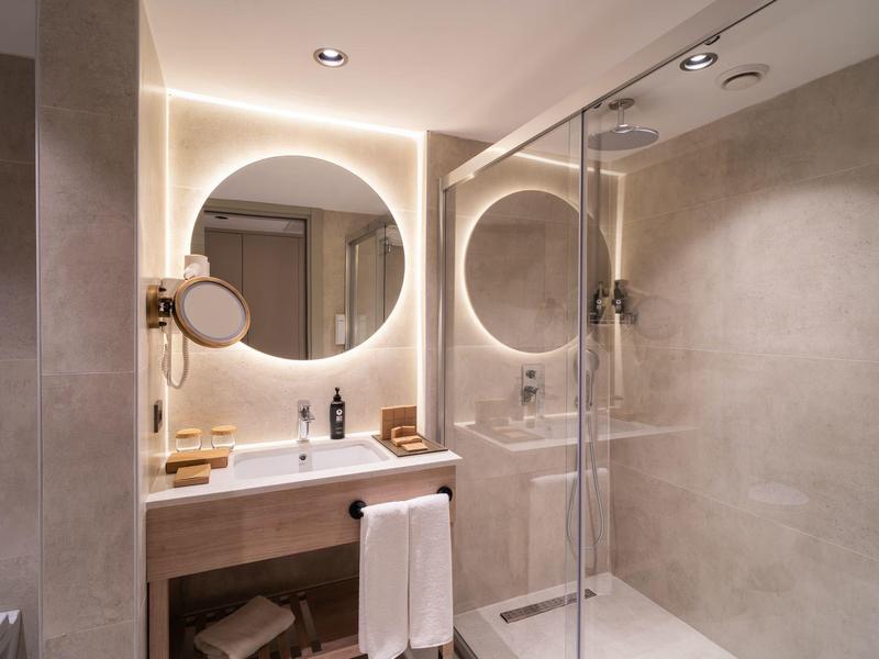 Modern bathroom with round mirror, washbasin, and large walk-in shower.