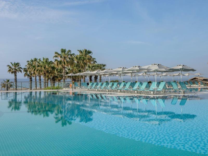 Large pool with lounge chairs and palm trees under a blue sky at a hotel beach.
