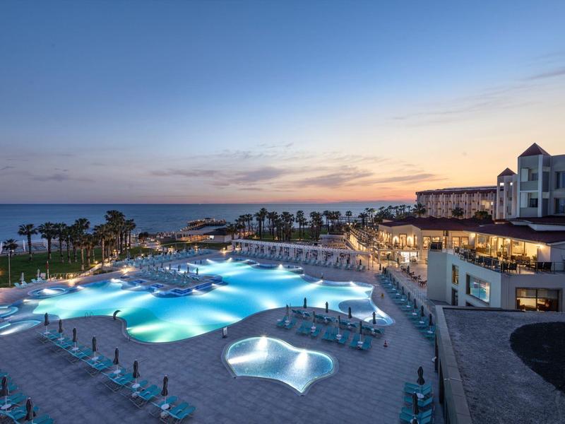 Large hotel resort with illuminated pool at dusk overlooking the sea.