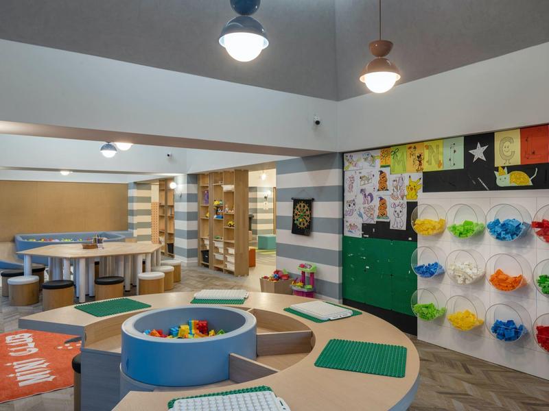 Colorful, modern kids' play area with climbing wall, ball pit, and seating inside a hotel space.