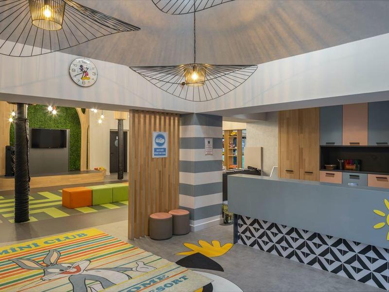 Modern hotel lobby with reception, colorful carpet, and seating area with shelves.