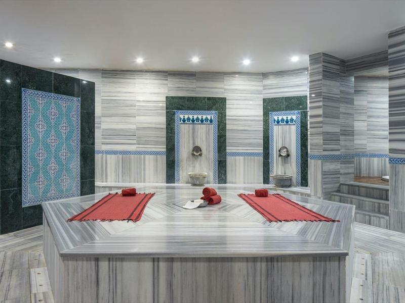 Modern hammam room with marble surfaces, basins, and red cushions