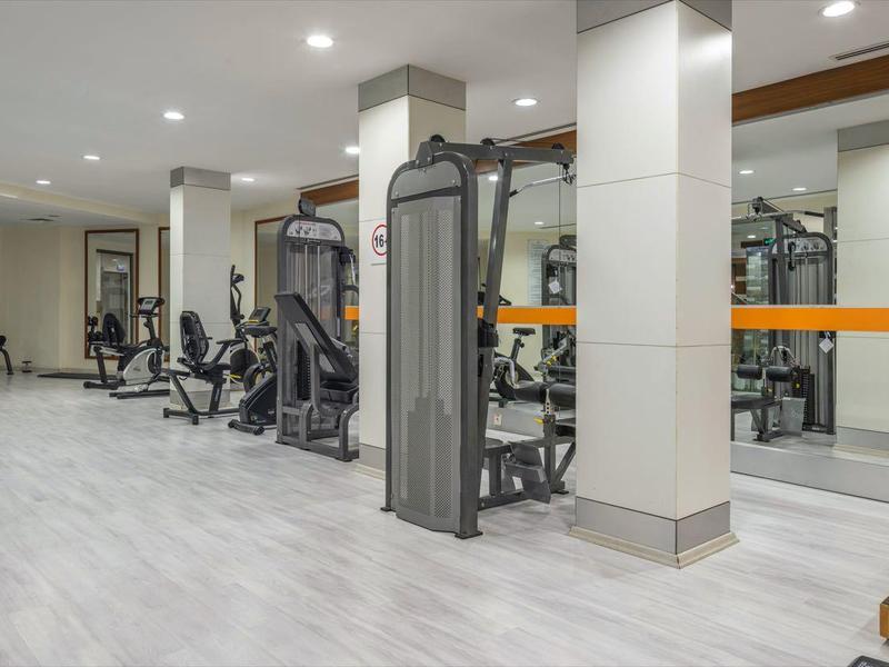 Modern gym with various workout machines and dumbbells in a bright room.