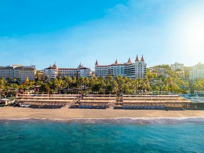 Luxusní hotel na pláži s palmami a čistým modrým mořem pod jasnou oblohou.