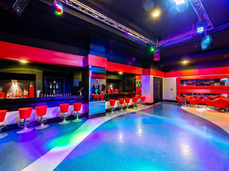 Barevný moderní bar s neonovými světly, stoličkami a posezením.