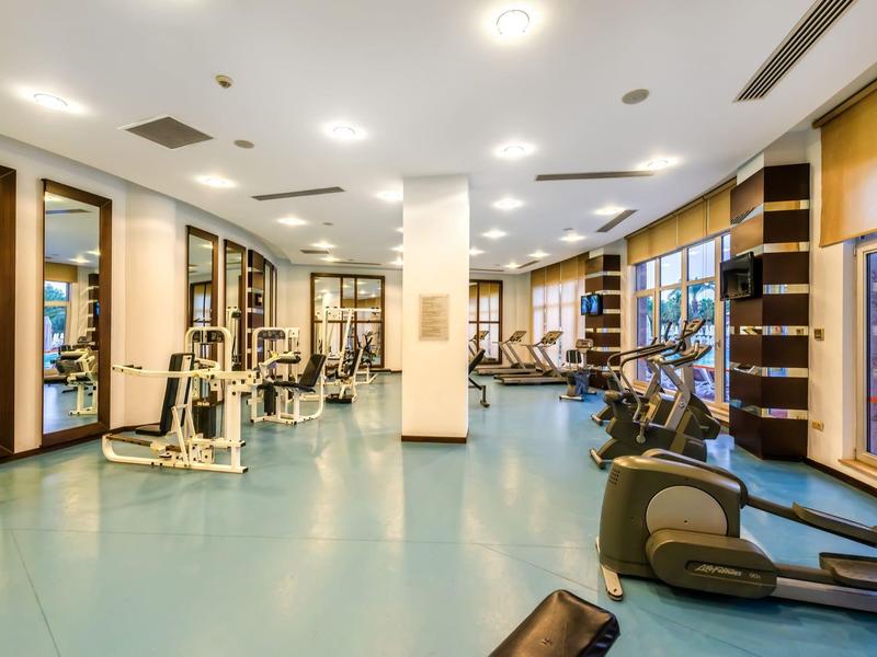 Prostorná posilovna s moderním vybavením a velkými okny pro přirozené světlo.