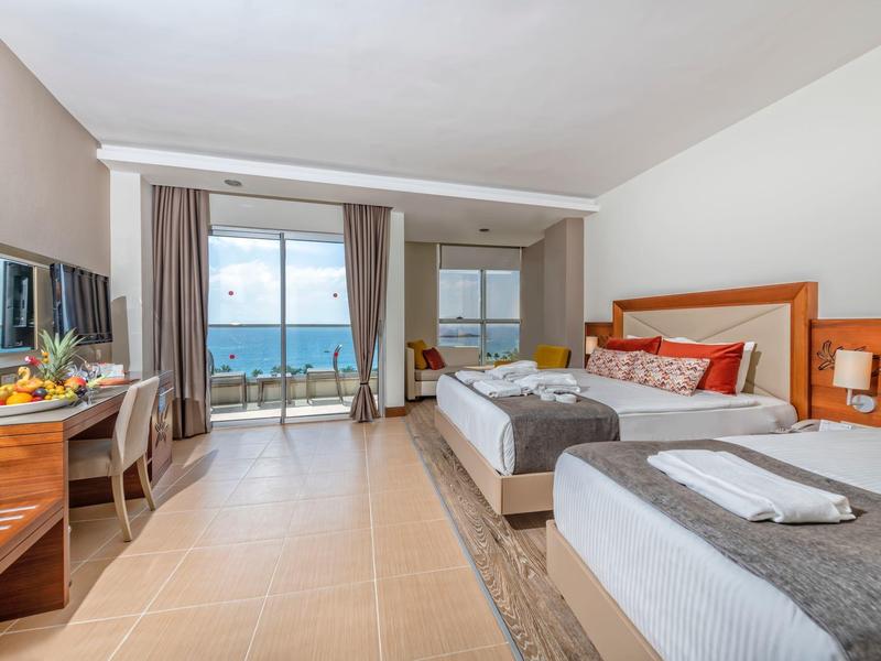 Světý hotelový pokoj se dvěma postelemi, balkonem s výhledem na moře a moderním zařízením.