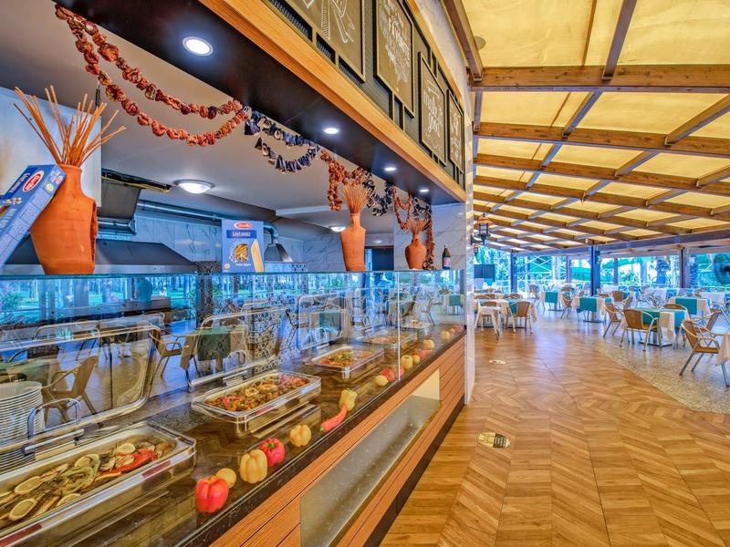 Prostorná hotelová restaurace s krytým posezením a skleněnou vitrínou s dezerty.