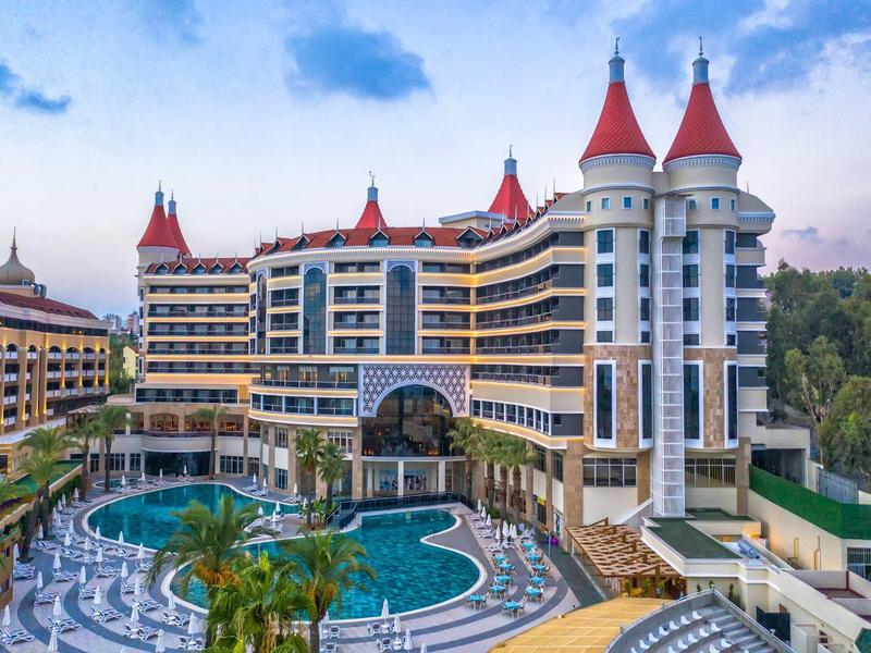 Velký hotelový resort s červenými věžemi, zakřivenými balkóny a bazénem před ním.