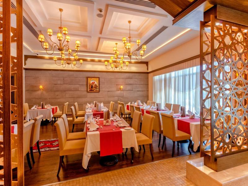 Elegantní hotelová jídelna s lustry, pečlivě prostřenými stoly a dekorativními dřevěnými příčkami.