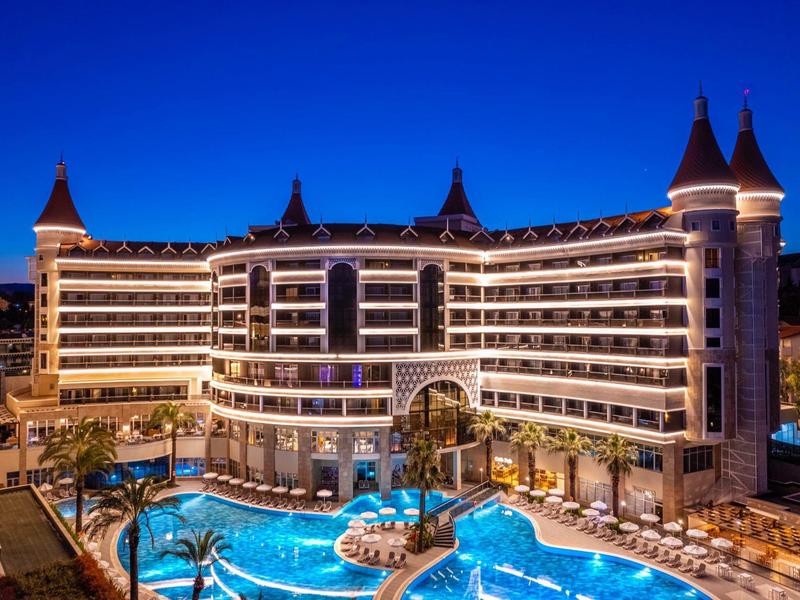 Luxusní hotel s osvětleným bazénem a palmami při západu slunce.