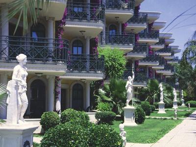 Edificio de hotel con balcones y jardín con estatuas y arbustos bien cuidados