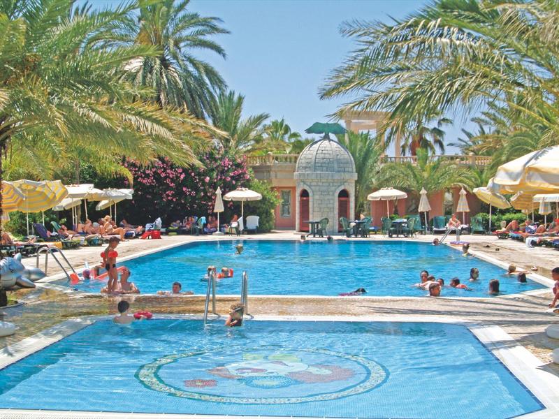 Dos piscinas con palmeras y sombrillas en un complejo hotelero tropical.