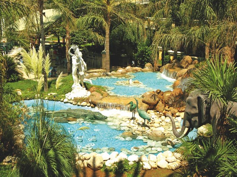Jardín paisajístico con estanques, estatuas y vegetación tropical en un resort vacacional.