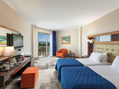 Lichte hotelkamer met twee bedden, stoelen en balkon met uitzicht op zee.