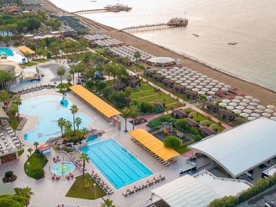 Luftaufnahme eines Resort mit Pools, Palmen, Liegestühlen und Strand am Meer.