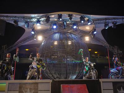 Motorijders poseren voor een grote verlichte wereldbol op een podium 's nachts