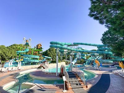 Uitzicht op een waterpark met glijbanen, zwembaden en bomen onder een heldere hemel.