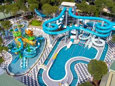 Velký vodní park s modrými tobogány, bazény a okolními odpočinkovými zónami v hotelovém komplexu.