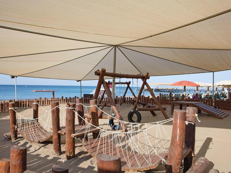 Überdachter Spielbereich am Strand mit Klettergerüst, Netzen und Schaukeln aus Holz.