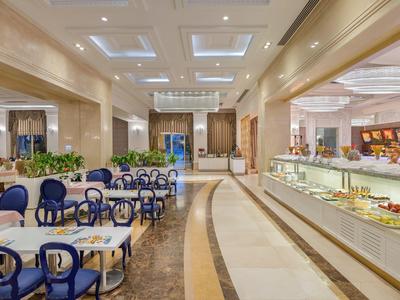 Großer Hotelrestaurantbereich mit hellen Wänden, blau gepolsterten Stühlen und einer Dessertvitrine.