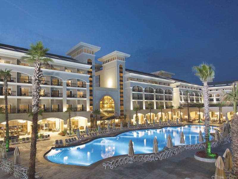 Großes Hotel mit beleuchtetem Pool und Palmen bei Nacht