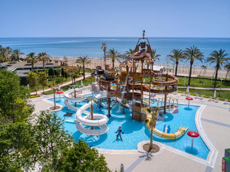 Wasserpark mit Rutschen und Spielplatz am Strand mit Palmen und Meer im Hintergrund.