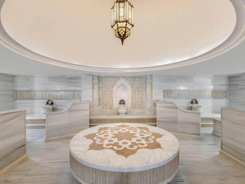 Luxuriöser Hammam mit zentralem runden Sitzplatz und kunstvollen Fliesen an der Wand.
