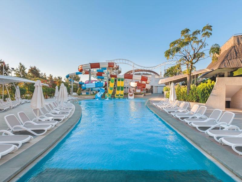 Ein Schwimmbecken mit Wasserrutschen und Reihen von weißen Liegestühlen an beiden Seiten.