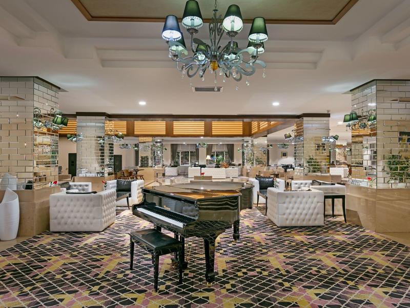 Elegante Hotellobby mit Klavier, Sitzecken und einem großen Kronleuchter in hellem Ambiente.