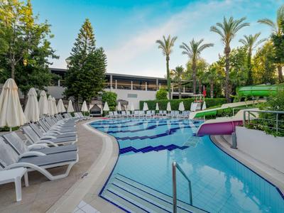 Outdoor hotel pool with lounge chairs and palm trees under clear sky.