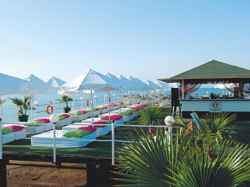 Plage avec parasols blancs et transats à côté d'un bar de plage sous un ciel clair.