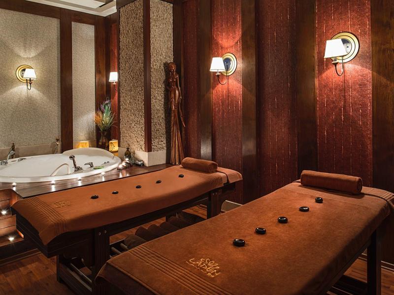 Salle de spa confortable avec tables de massage et grand jacuzzi sous une lumière chaude.