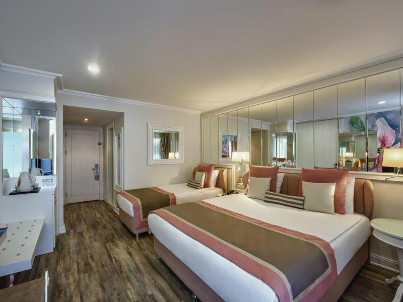 Chambre d'hôtel lumineuse avec un lit double, un sol en bois et de grands miroirs muraux.