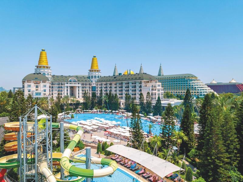 Grand hôtel avec tours jaunes, piscine et toboggans entouré d'arbres.