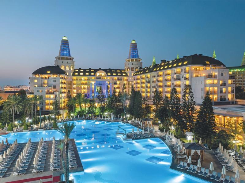 Hôtel de luxe avec piscine éclairée et nombreux transats au crépuscule.