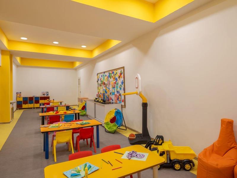Salle de jeux pour enfants colorée avec tables, chaises, jouets et poufs confortables dans un cadre hôtelier.