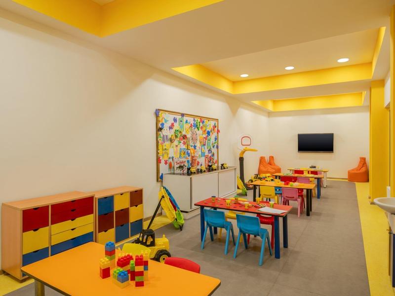 Salle de jeux colorée pour enfants avec tables, chaises et jouets dans un hôtel.