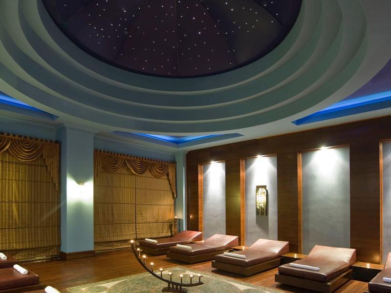 Salle de détente moderne avec éclairage circulaire au plafond et fauteuils marron sur sol en bois.