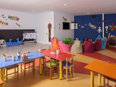 Hell eingerichteter, großer Kindergartenraum mit bunten Tischen, Stühlen, Spielsachen und gemütlicher Sitzecke.