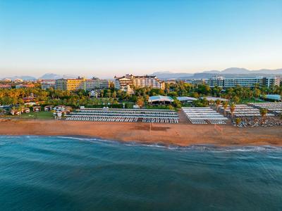 Blick auf einen breiten Sandstrand mit Liegen vor Hotels und Gebäuden an der Küste.