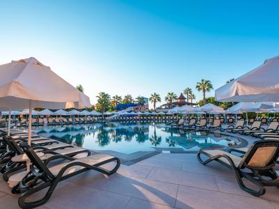 Großer Poolbereich mit Liegestühlen und Sonnenschirmen in einem sonnigen Hotelresort.