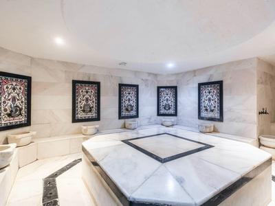 Luxuriöser Hamam mit Marmorbecken, Wandsäulen, kunstvollen Wandpaneelen und sanfter Beleuchtung.