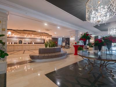 Große Hotellobby mit glänzendem Boden, Sitzbereich, Empfangstheke und modernen Kronleuchtern.