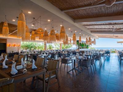 Spacious restaurant with wooden tables, woven lamps, and a sea view.