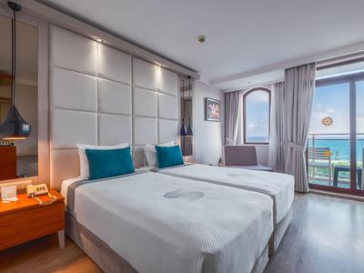 Modern hotel room with two single beds, desk, and balcony overlooking the sea.