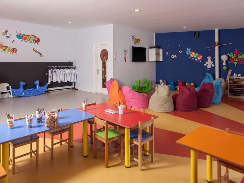 Sala de jardín infantil colorida y espaciosa con casita de juegos, mesas y sillas para niños.