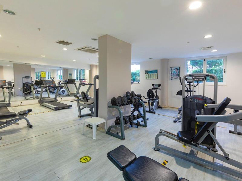 Gimnasio moderno con máquinas y pesas, suelos claros y ventanas grandes para luz natural.