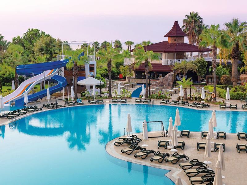 Gran piscina de hotel con toboganes de agua, tumbonas y vegetación tropical al atardecer.